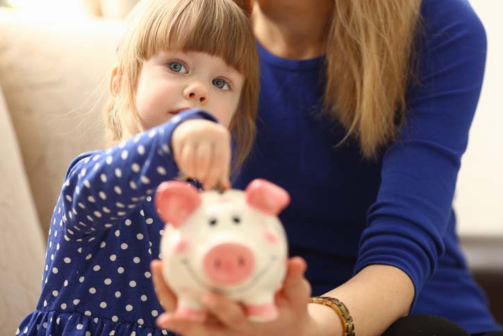 Child contributing to savings by placing money in piggy bank