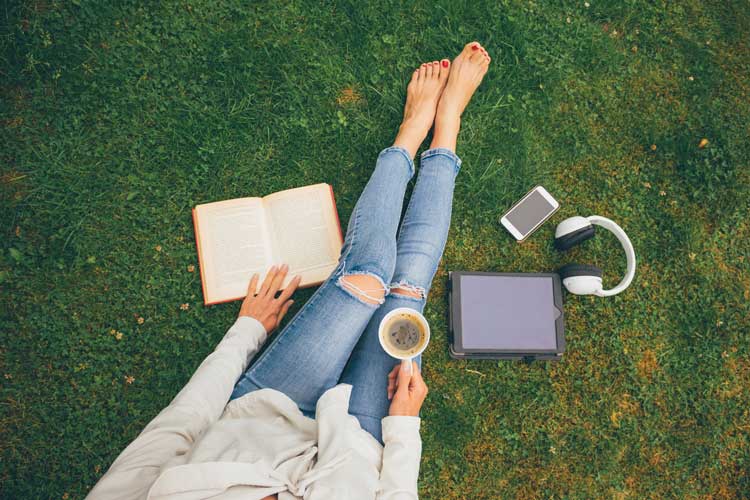 Student reading on lawn with a coffee