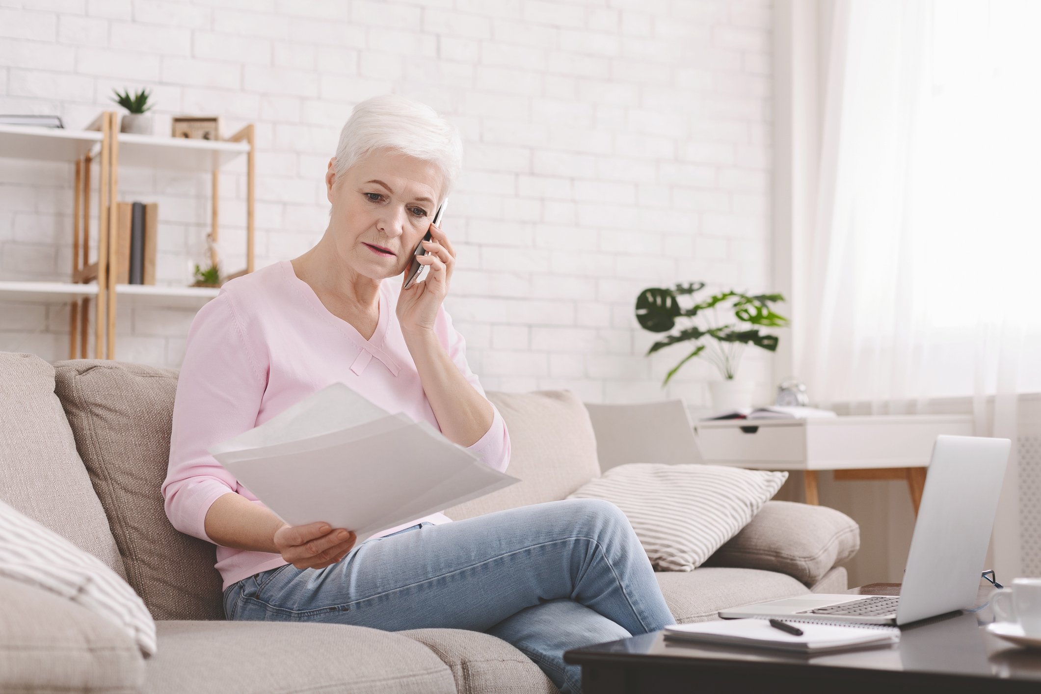 Senior sitting on couch reviewing bills while talking on the phone